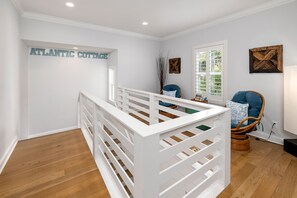 Una stanza con una culla bianca, una sedia in vimini e un cartello appeso al muro con la scritta "ATLANTIC COTTAGE".