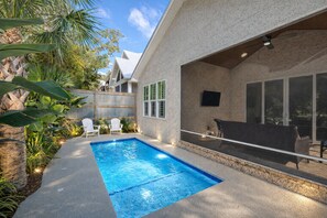 Un jardin avec une piscine, un espace salon extérieur et une terrasse couverte.