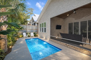 A backyard with a swimming pool, outdoor seating, and a covered patio area.