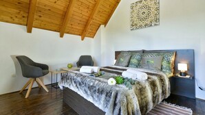 Un dormitorio con techo de madera, una cama con manta de piel, dos sillas, una mesita de noche y un adorno en la pared.