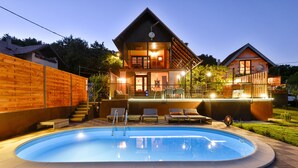 Una casa de dos pisos con piscina, fachada de madera y un patio bien iluminado.