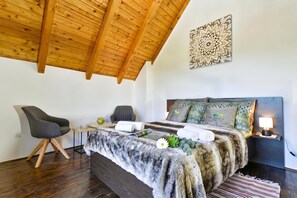A bedroom with a wooden ceiling, a bed with patterned pillows, a desk with a chair, and a nightstand with a lamp.