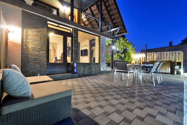 A modern outdoor patio with a checkered floor, a seating area with cushions, and a dining setup.