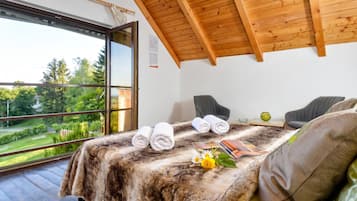 Une chambre avec une grande fenêtre, un lit avec des serviettes pliées, une petite table avec un vase et une chaise.