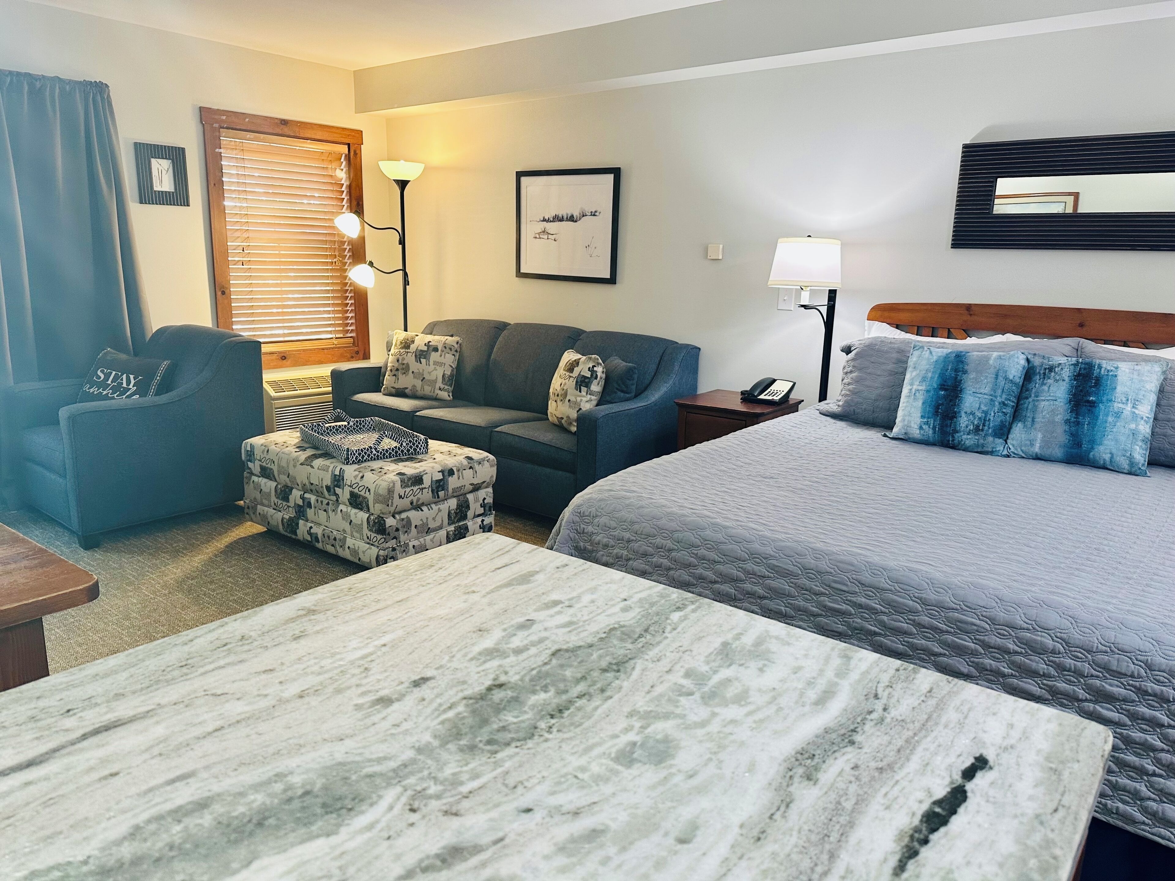 A hotel room with a bed, a sofa, a chair, a small table, and a lamp.