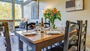 A dining area with a wooden table set for four, a vase with flowers, and a bottle of wine. - Greystone Lodge 318 Ski-in/Out by Acer Vacations (Whistler)