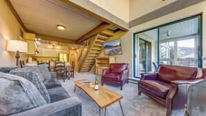 A spacious living area with a wooden ceiling, a staircase, and a large window with a view. - Greystone Lodge 318 Ski-in/Out by Acer Vacations (Whistler)
