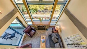 A high-ceilinged room with a fireplace, seating area, and large windows. - Greystone Lodge 318 Ski-in/Out by Acer Vacations (Whistler)