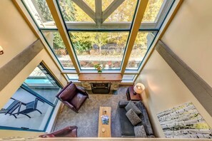 A high-ceilinged room with a fireplace, seating area, and large windows.