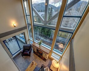 A high-ceilinged room with a fireplace, a seating area, and large windows offering a view of a snowy landscape.