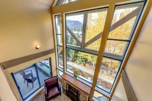 A high-ceilinged room with large windows, a fireplace, and a view of a mountainous landscape.