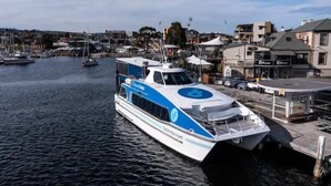 A modern ferry docked at a marina with a cityscape in the background.