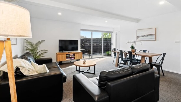A modern living room with a sofa, a coffee table, a TV, and a dining area with chairs and a table.