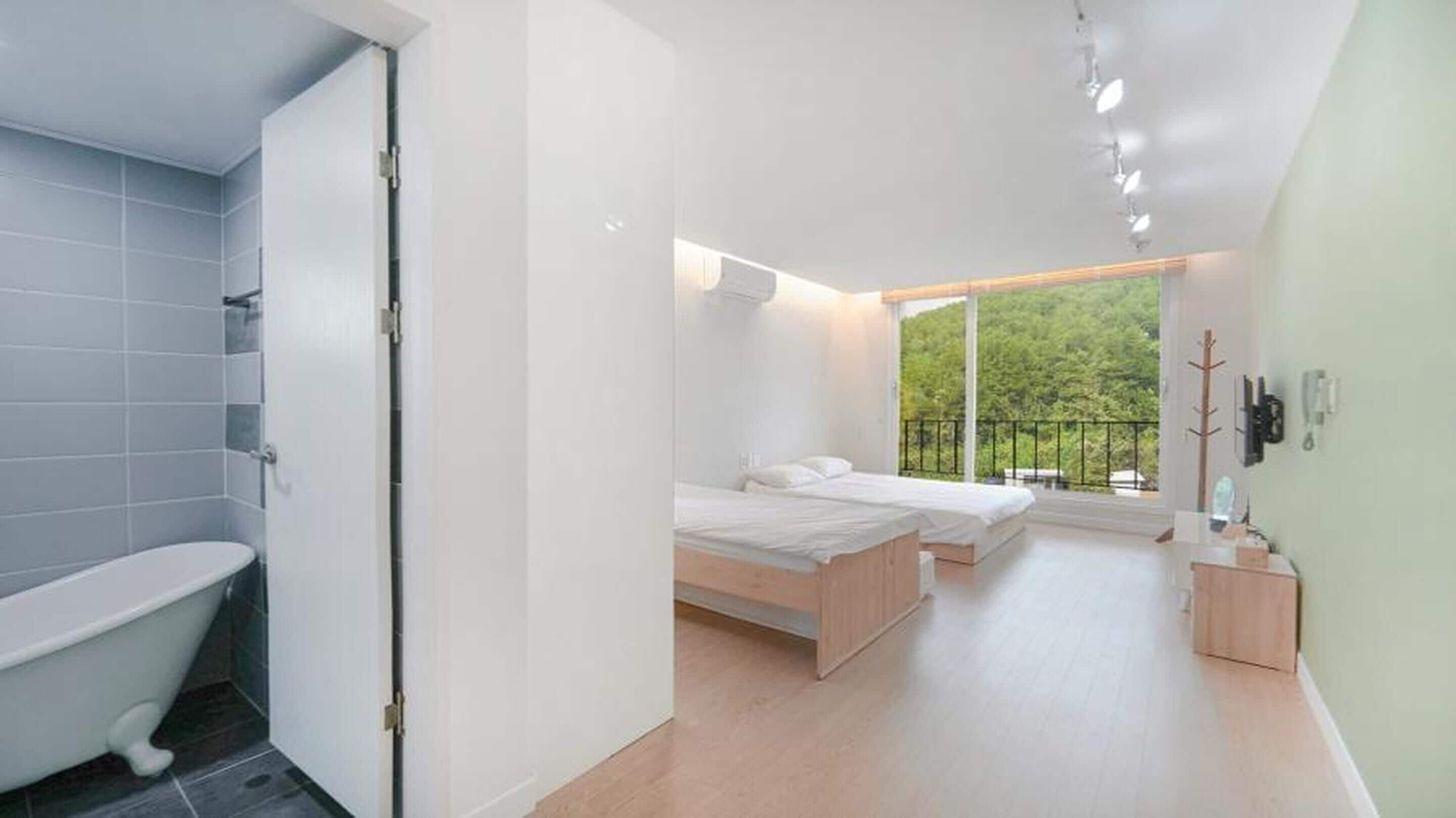 Un dormitorio moderno con un ventanal grande, una cama, una mesita de noche y un baño con bañera e inodoro.