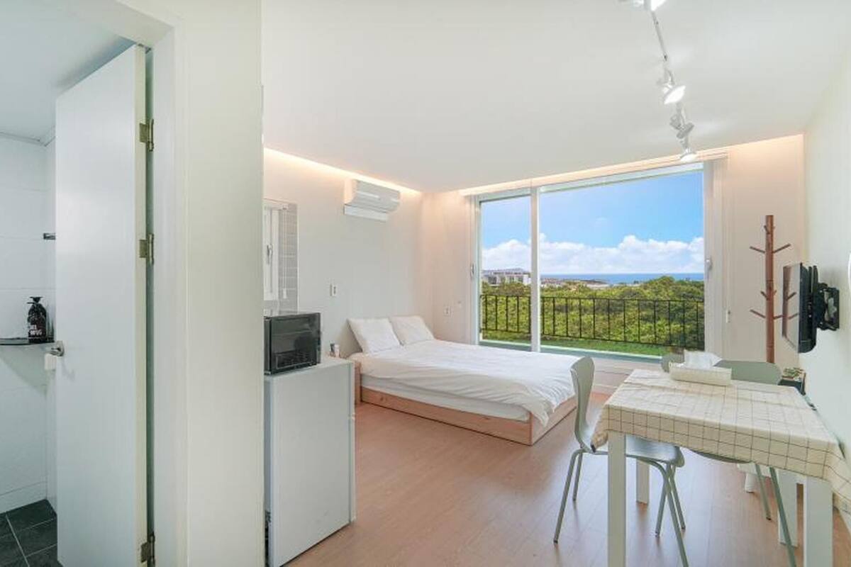 Een slaapkamer met een bed, bureau en stoel, een kleine kitchenette en een balkon met uitzicht.