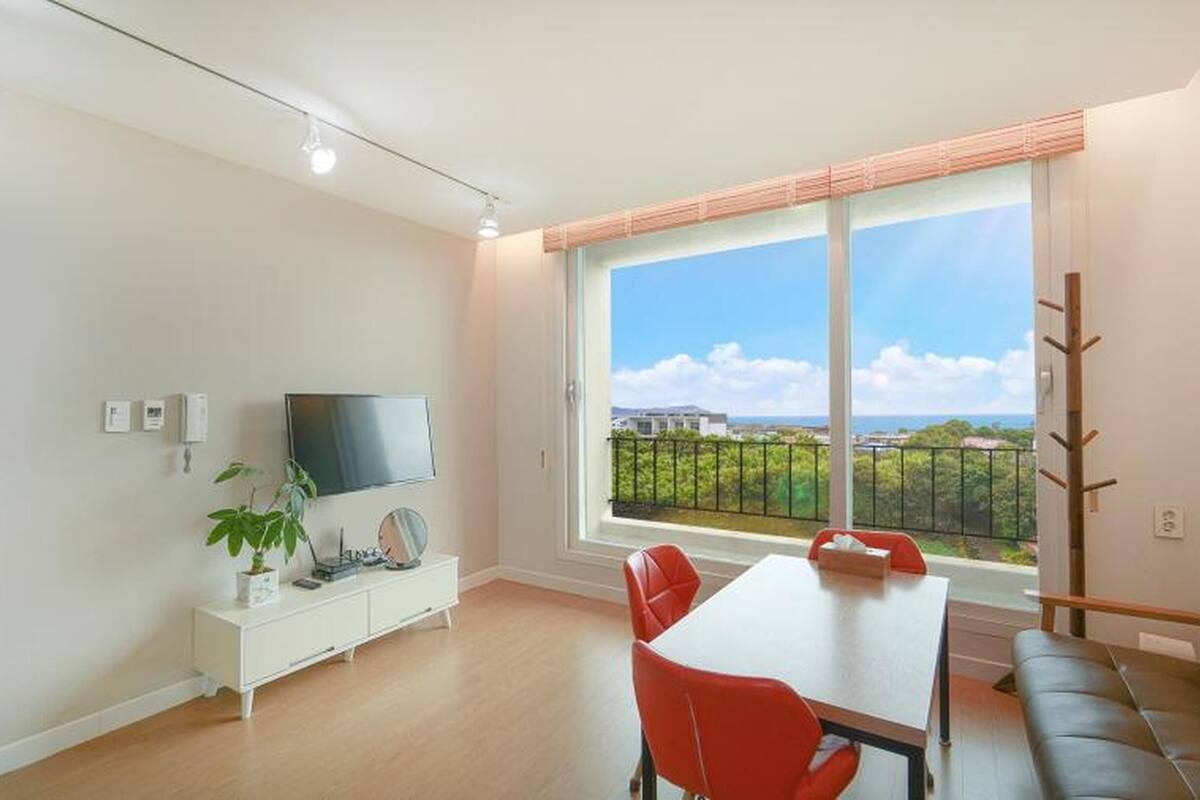 Een moderne woonkamer met een groot raam, een flatscreen televisie, een eettafel met stoelen en een bank.