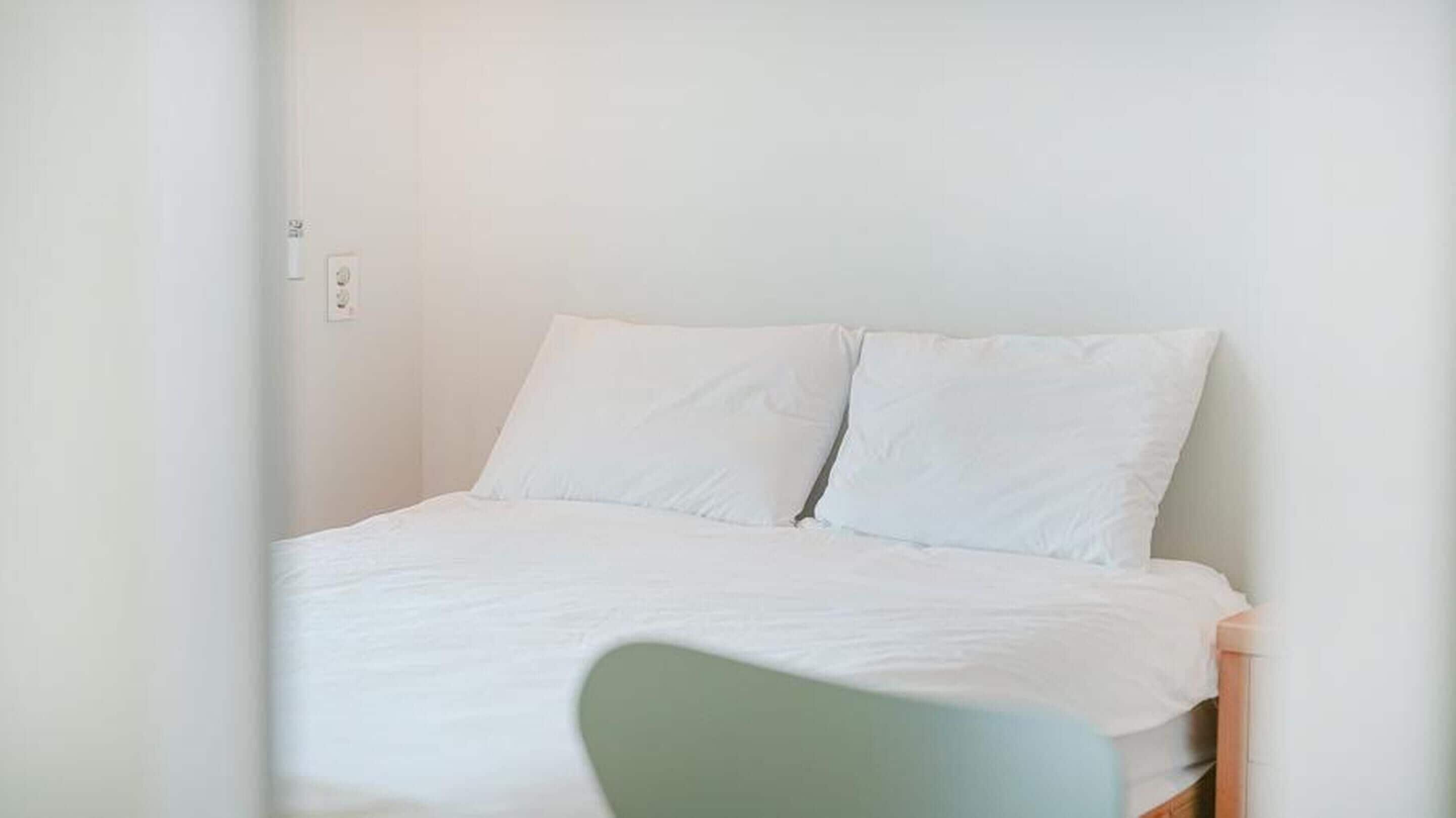 A simple, clean room with a bed, a chair, and a light switch on the wall.