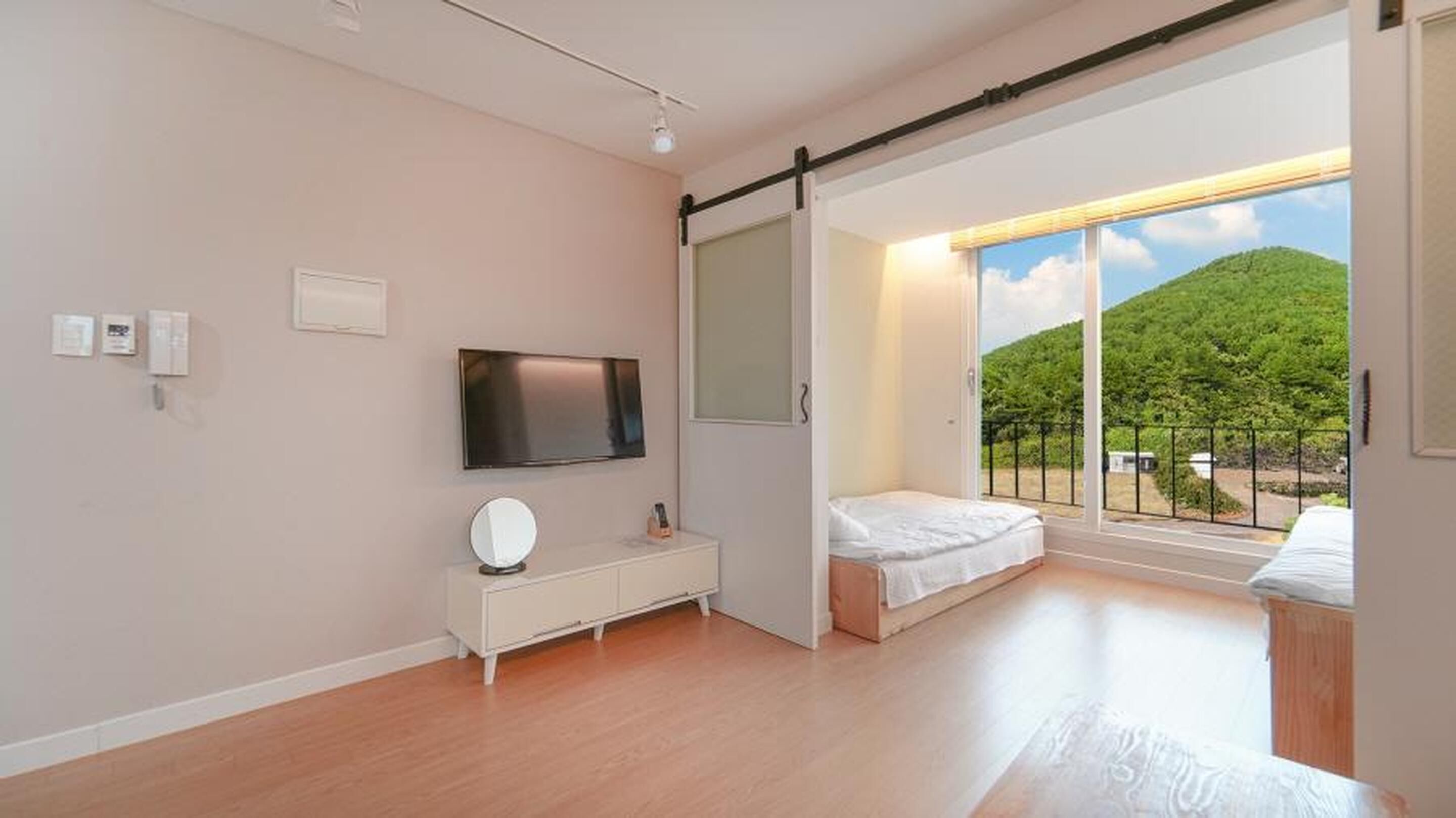 A modern bedroom with a large window, a flat-screen TV, a bedside table, and a bed.