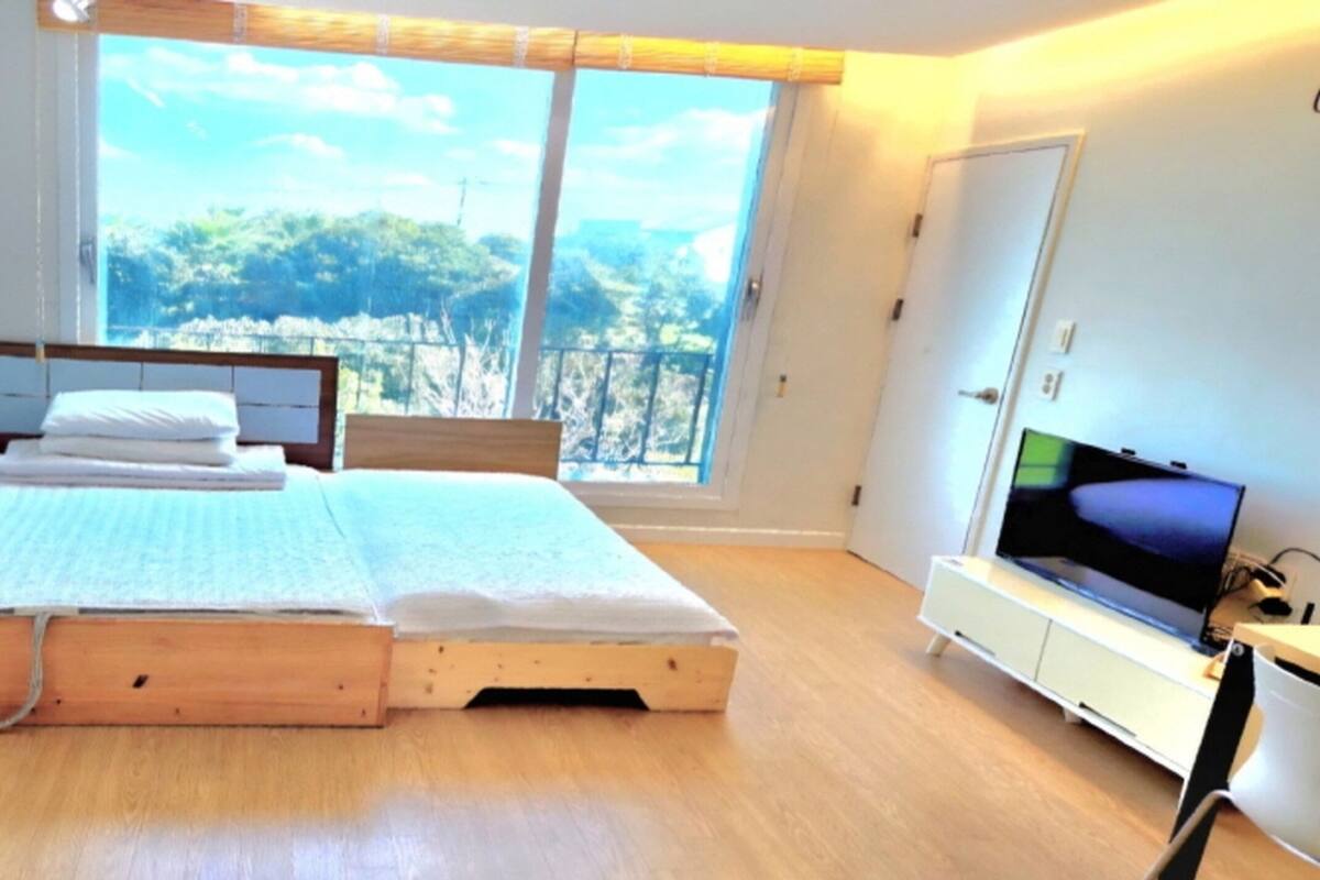 Een slaapkamer met een bed, een televisie en een raam met uitzicht op bomen.