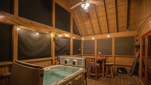 Un jacuzzi en una cabaña de madera con una mesa, sillas, ventanas amplias y un ventilador de techo.