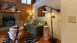 Interior acogedor de una cabaña con chimenea de piedra, techo de madera y un rincón de comedor con una mecedora.