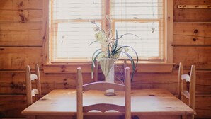 Et træspisebord med fire stole, en vase med blomster og et vindue med persienner.