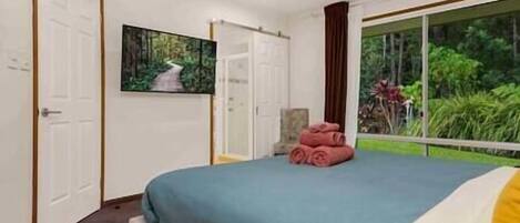Un dormitorio con cama, un cuadro, una silla y una ventana con vistas a zonas verdes.