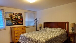 Un dormitorio con cama de madera, cómoda, un cuadro en la pared y una lámpara en la mesita de noche.