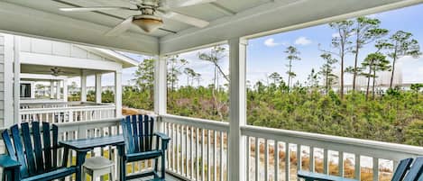 A covered outdoor area with a ceiling fan, a table with chairs, and a view of the surrounding landscape.
