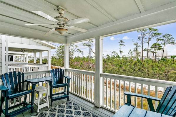 A covered outdoor area with a ceiling fan, a table with chairs, and a view of the surrounding landscape.