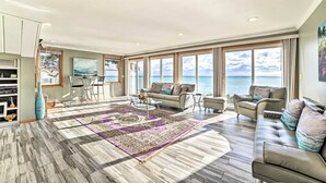 Un ampio soggiorno con una grande finestra vista mare, un divano moderno e un tavolino da caffè con oggetti decorativi.