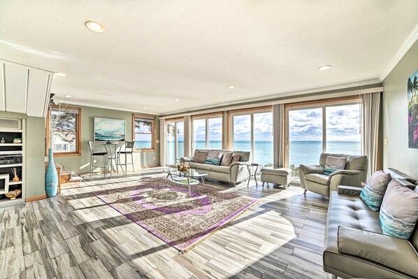 Amplia sala de estar con un gran ventanal con vistas al mar, un moderno conjunto de sofás y una mesa de centro con objetos decorativos.