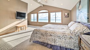 Una camera da letto con un letto grande, un ventilatore a soffitto, una TV e vista sull'oceano attraverso ampie finestre.