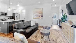A modern living room with a black leather sofa, a coffee table, and a kitchen area with white cabinets and a microwave. - Cozy & Stylish 3BD near LSU (Baton Rouge)