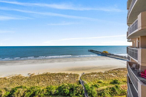 A beach view from a balcony with a pier extending into the ocean.