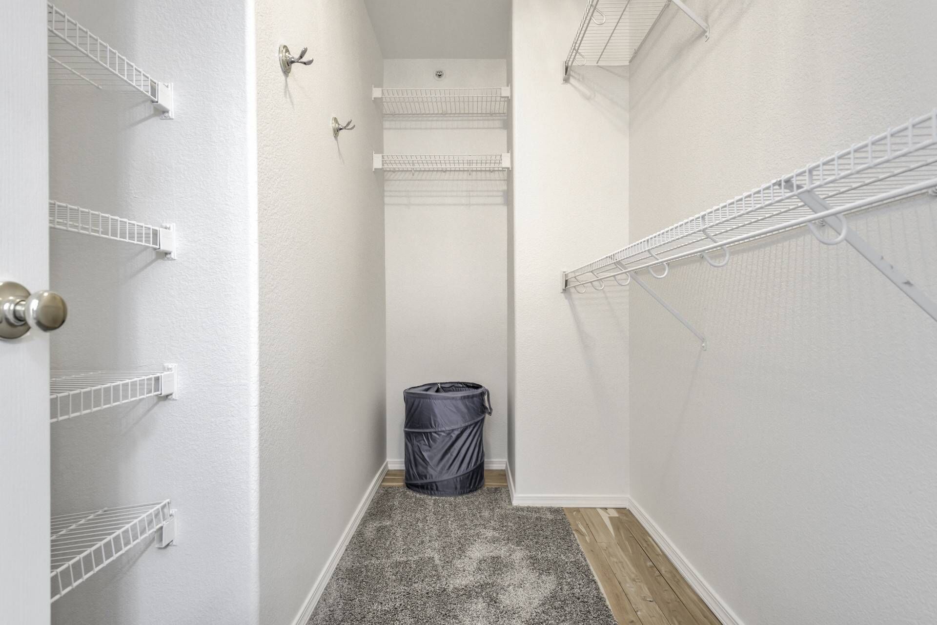 A narrow hallway with white walls, a wooden floor, and metal wire shelves on both sides.