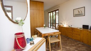 Una cocina con una mesa de madera, sillas, un florero rojo y un espejo.