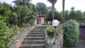 Una escalera de piedra conduce a un edificio de fachada rosa, rodeado de abundante vegetación y palmeras.