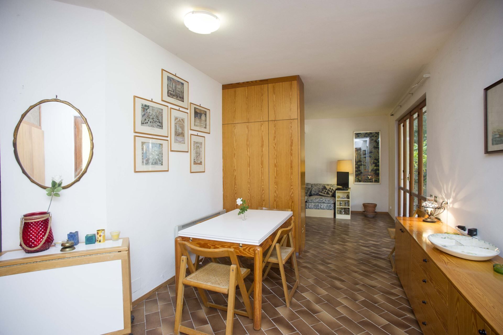 Un coin repas avec une table en bois, des chaises et un miroir. Des tableaux encadrés ornent le mur et une plante en pot est posée sur la table.