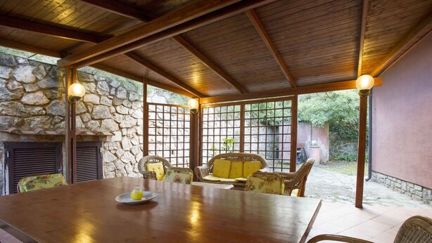 Un patio techado con pared de piedra, techo de madera y mobiliario de mimbre.