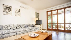 Una sala de estar con un sofá, un televisor, una mesa de madera y un ventanal corredizo que da a un espacio exterior.