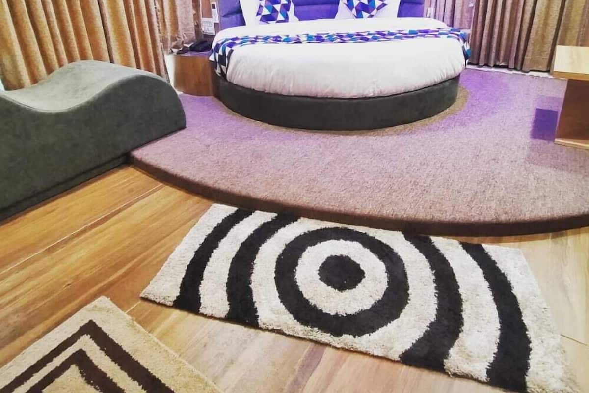 A bedroom with a round bed, purple curtains, and a patterned rug.