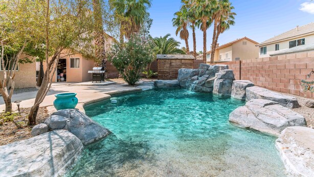 Un patio trasero con piscina, palmeras y un muro de ladrillo.