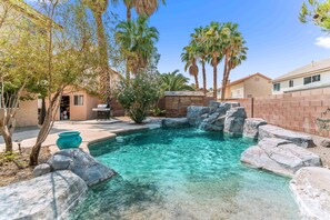 Ein Garten mit Swimmingpool, Palmen und einer Backsteinmauer.