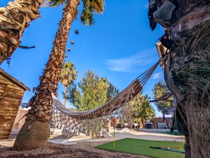 A hammock between palm trees in a backyard with a wooden building and a green lawn. - Amazing 5 BDR, Resort Style Pool w/Heater and Games. (Henderson)