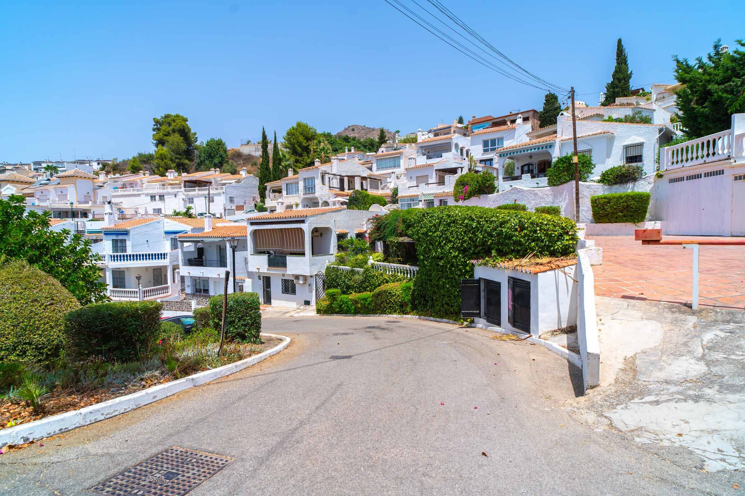 Une rue résidentielle bordée de maisons blanches, avec une chaussée pavée et un ciel dégagé.
