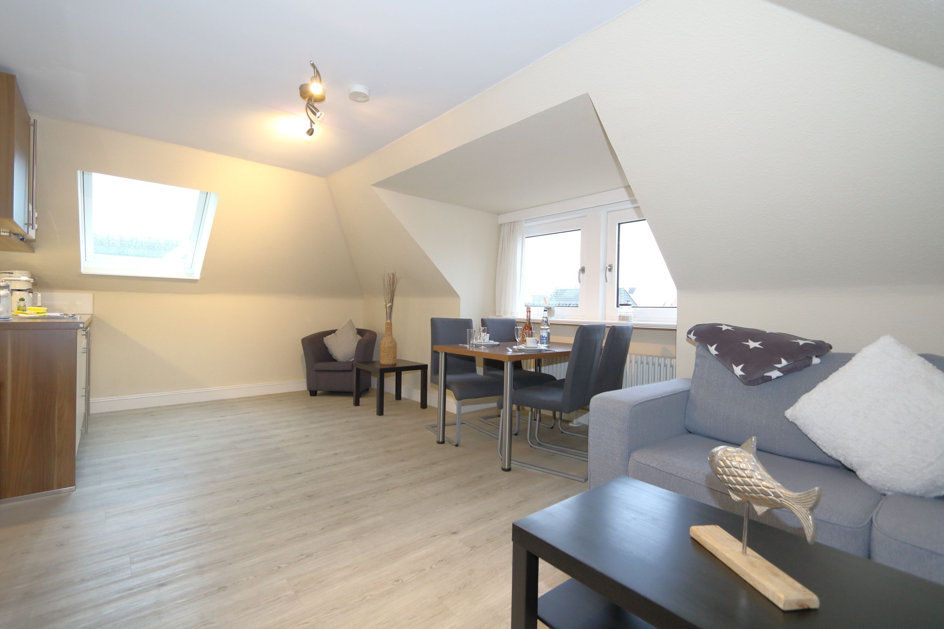 A modern living room with a dining area, a loft bedroom with a sloped ceiling, and a view of the city.