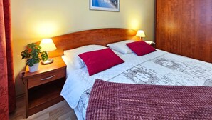 Ein ordentlich bezogenes Bett mit zwei Kissen, ein Nachttisch mit Lampe, ein gerahmtes Bild an der Wand und ein Holzschrank.