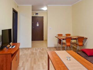 A compact living space with a wooden desk, a television, a dining table with chairs, and a sofa with a red pillow. - Naut 305 - Nautilius (Swinoujscie)