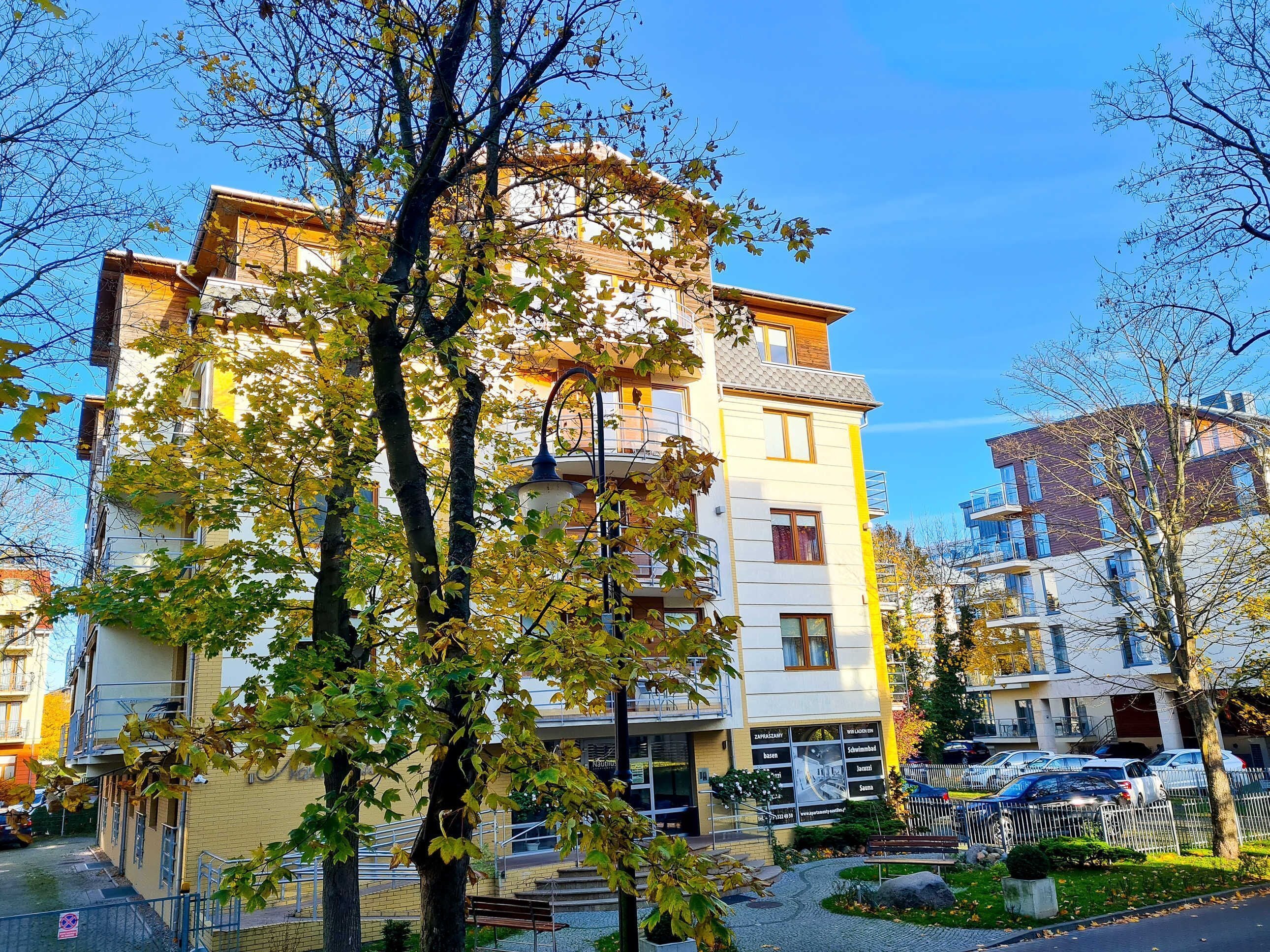 A multi-story residential building with balconies, a paved courtyard, and a parking area.